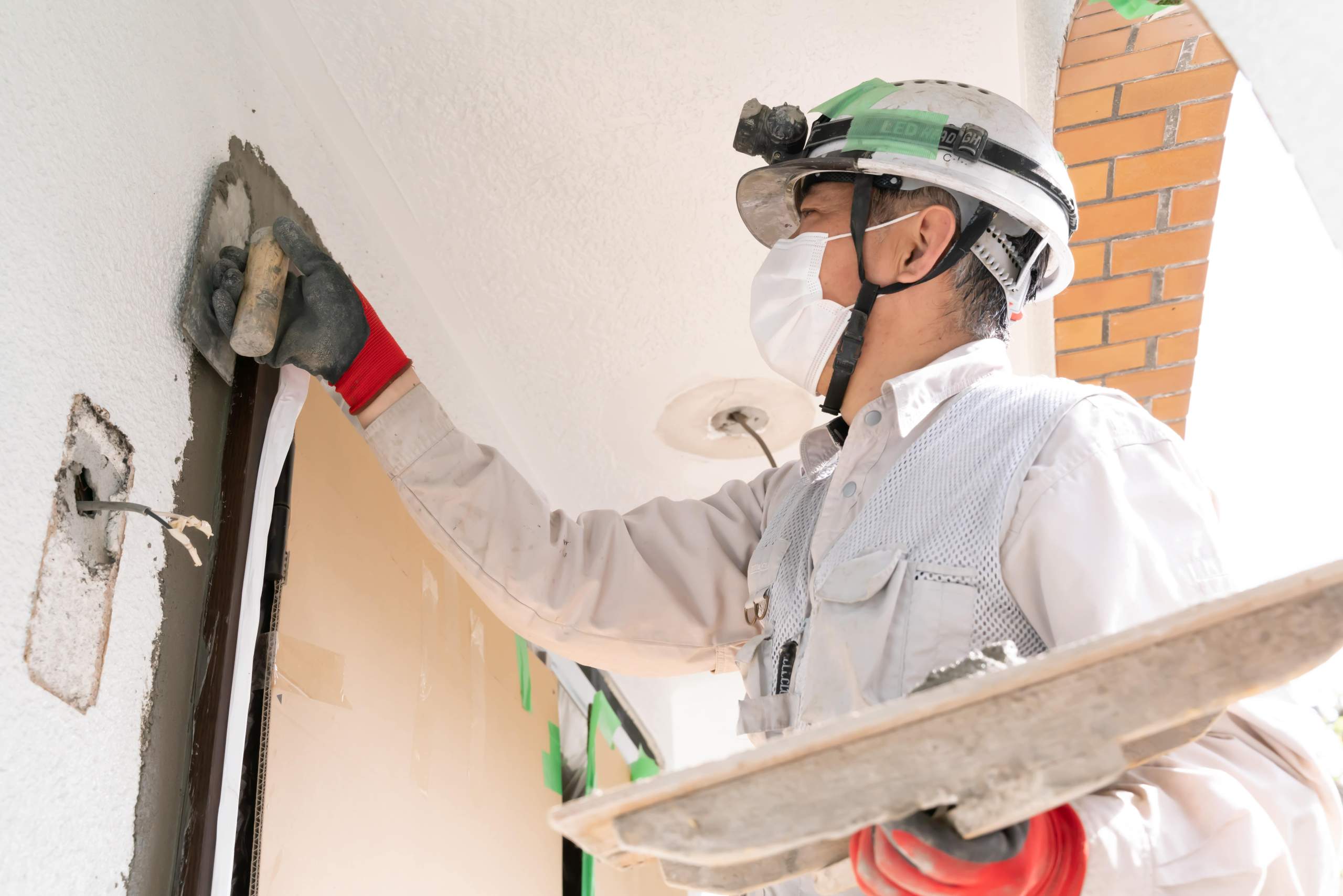ヘルメットとマスクを着用し、建物の壁の左官工事を行っている作業員